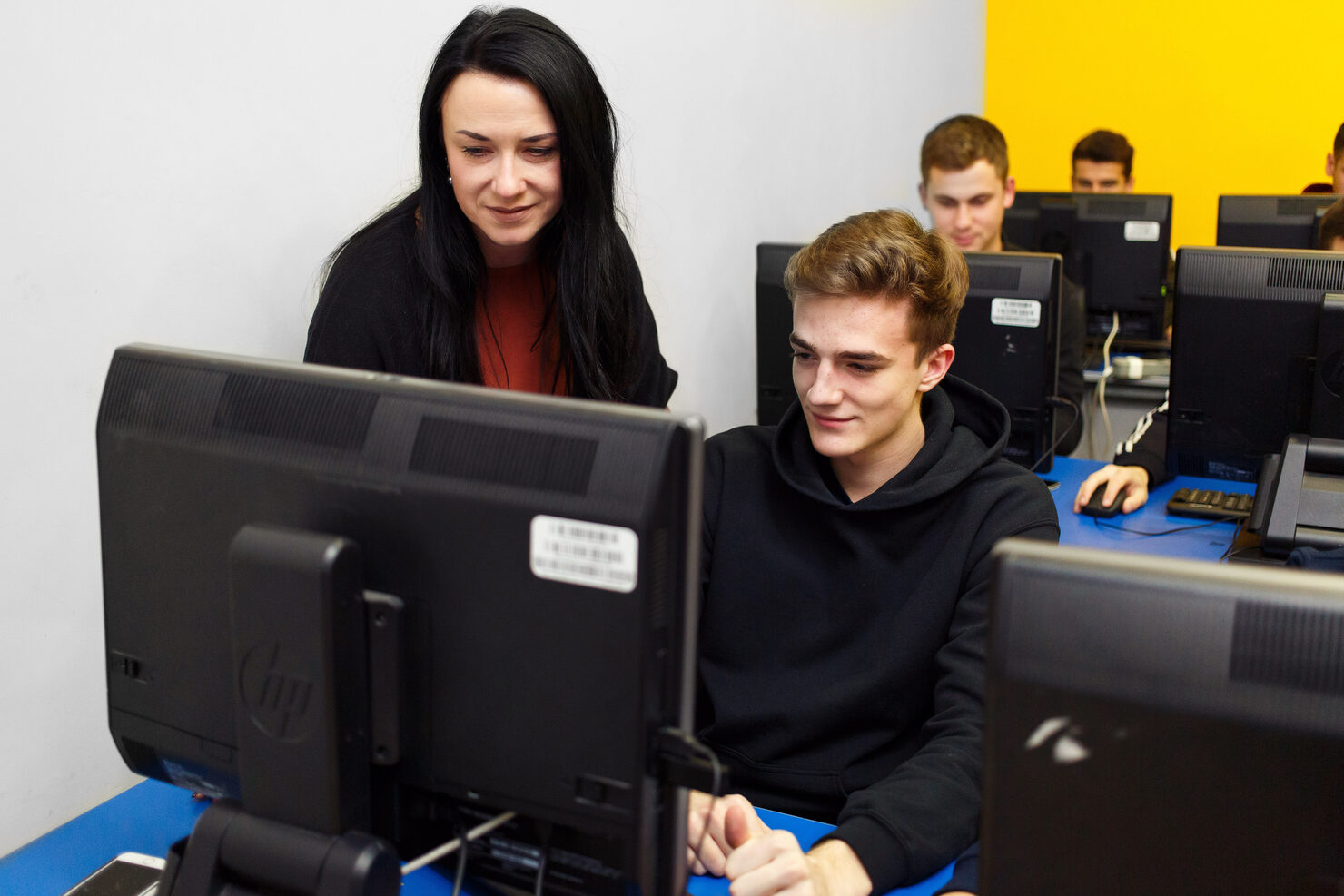 Преподавательница помогает студенту за компьютером в классе академии